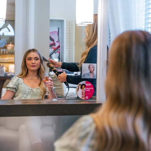 a woman holding a class of rosé while getting her hair curled