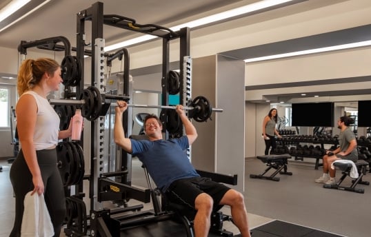 a woman spotting a man while he lifts a large weight