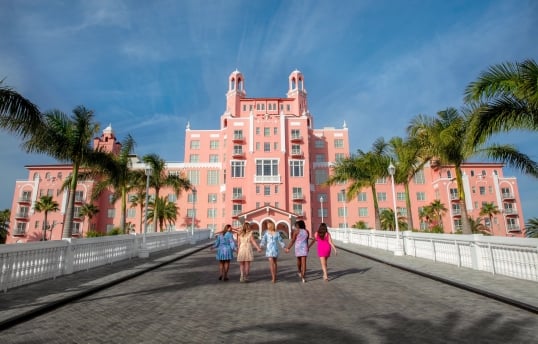 five women holding hands walking to the entrance of a hotel