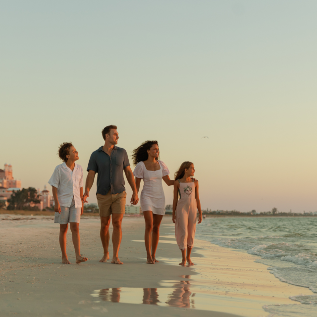 Family of four walking along the beach hand-in-hand at sunset, waves at their feet.
