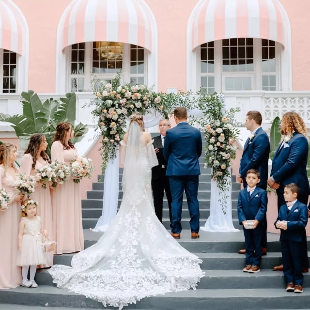 bride and groom getting married on a staircase with their wedding party standing behind them