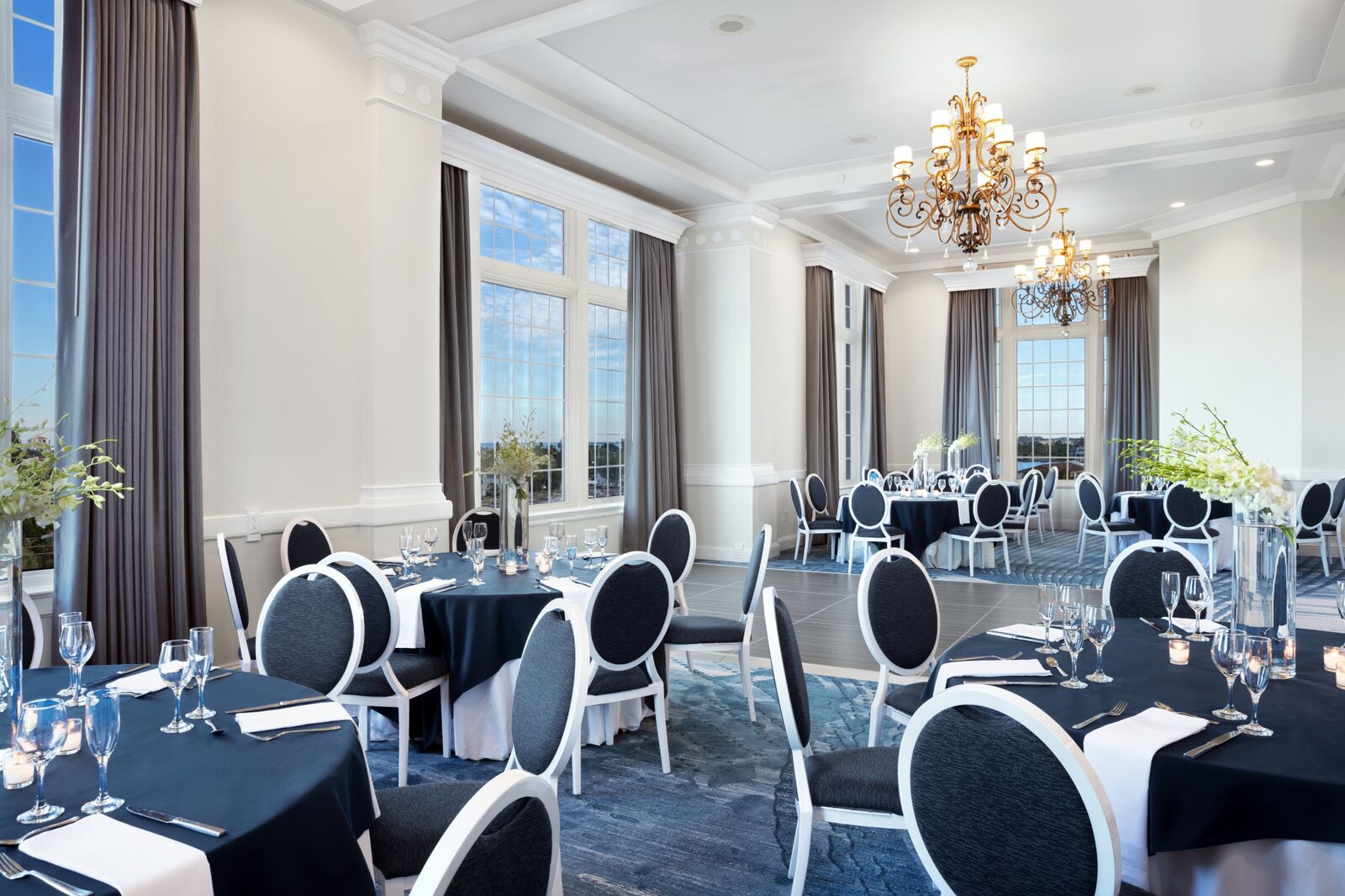 A spacious banquet room featuring blue tablecloths and white serviettes elegantly arranged on the tables.