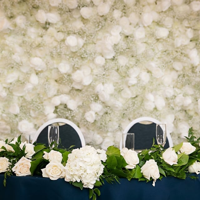 A table adorned with white flowers on a blue tablecloth with a white flower backdrop, creating a fresh and vibrant atmosphere.
