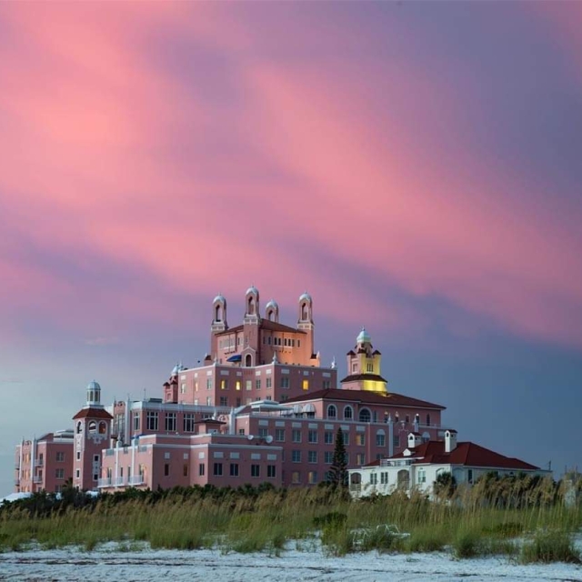 A pink building on the beach glows in the warm hues of a sunset, creating a serene coastal scene.