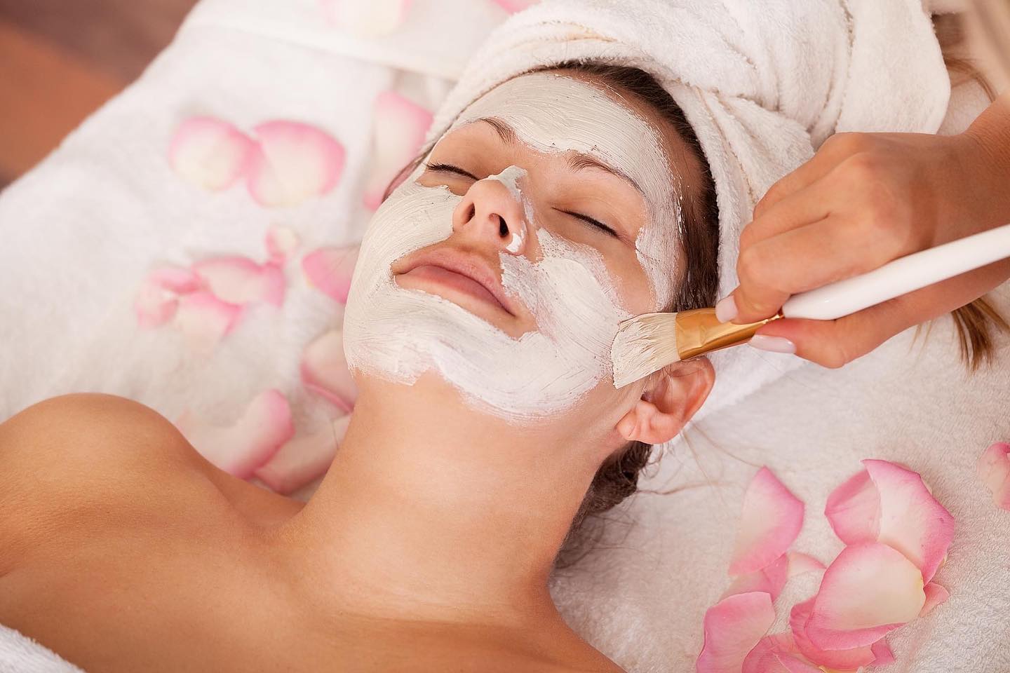A woman enjoys a facial treatment surrounded by delicate rose petals, promoting relaxation and rejuvenation.