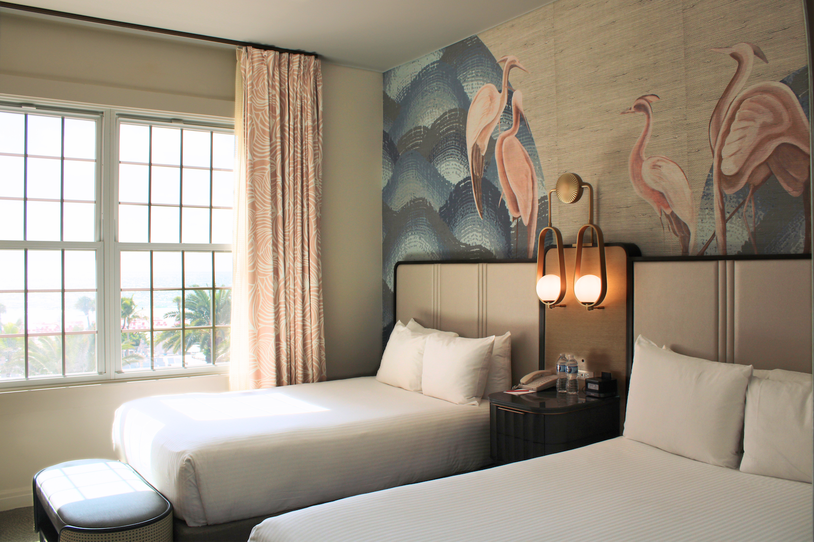 Hotel room with two twin beds, white linens, and a pink flamingo mural behind the headboard.