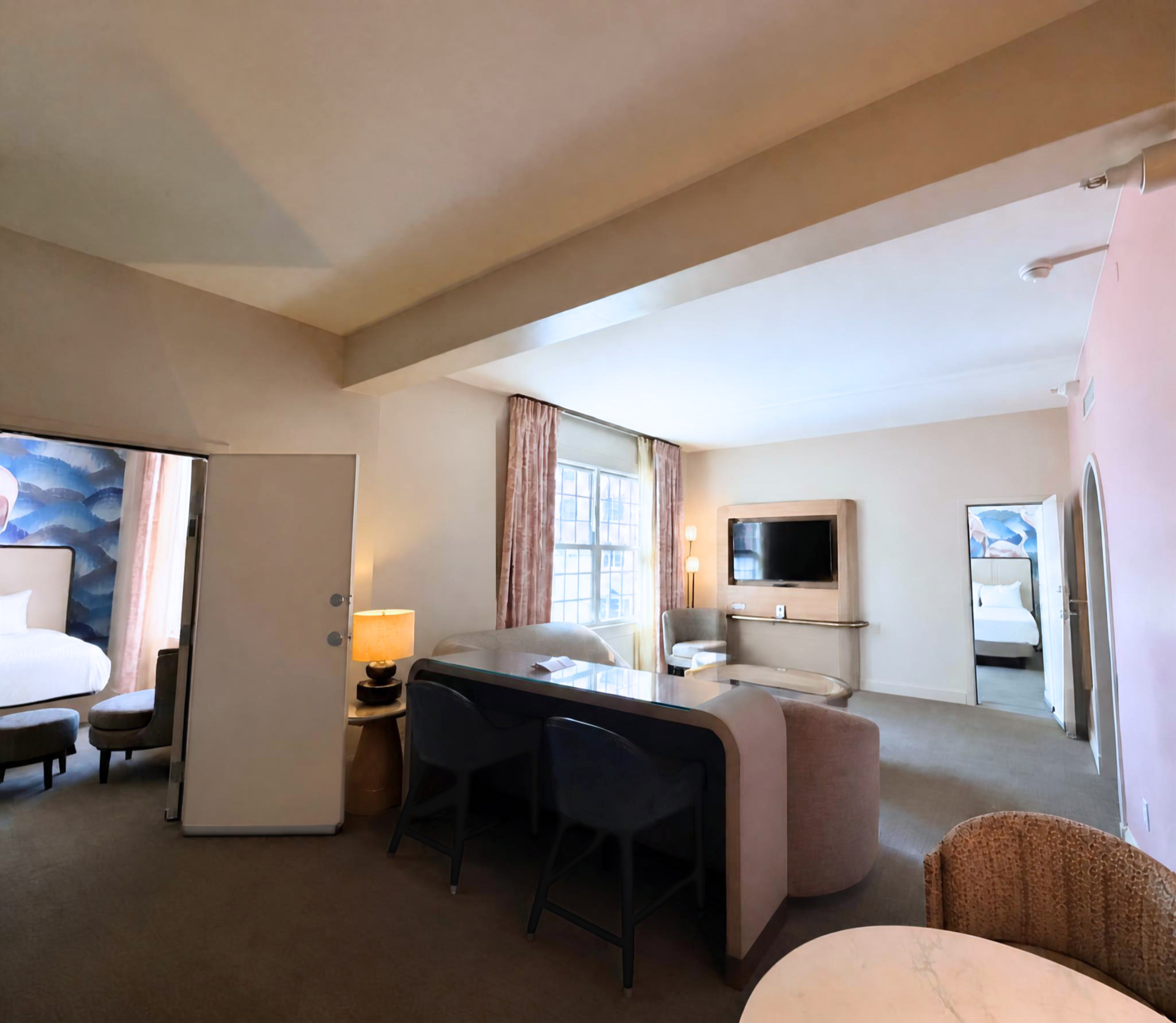 Hotel-style living area with pink walls, curved white coffee tables, and black chairs in a showroom-like lounge.
