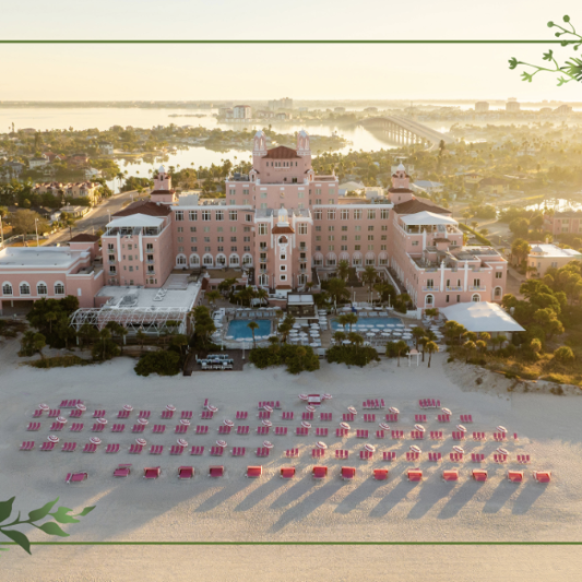 Aerial view of a pink seaside hotel at sunset, with rows of red sun loungers lined on the sand and decorative holiday border corners.