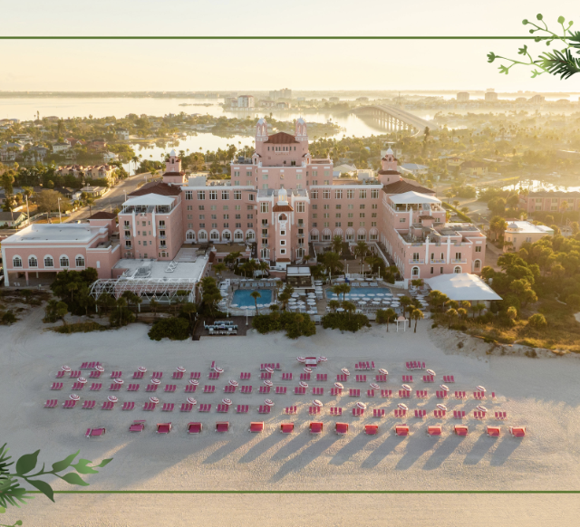 Aerial view of a pink seaside hotel at sunset, with rows of red sun loungers lined on the sand and decorative holiday border corners.