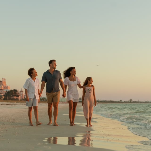 A family of five walking hand in hand along a beach at sunset.