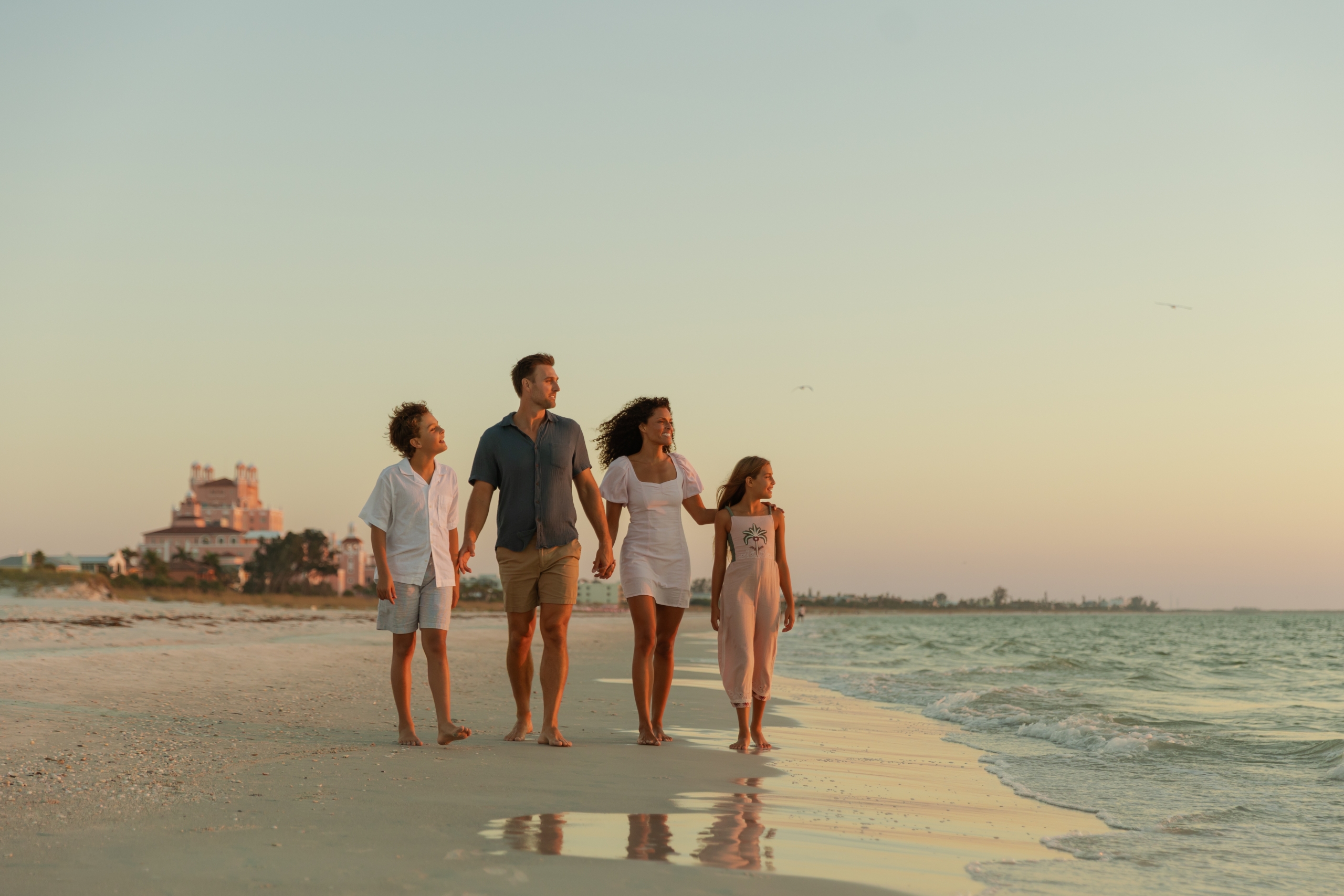 A family of five walking hand in hand along a beach at sunset.